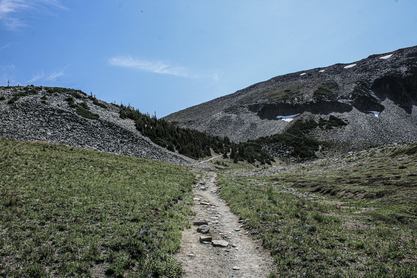 A hiking trail climbs through rocky mountain terrain toward distant peaks.
