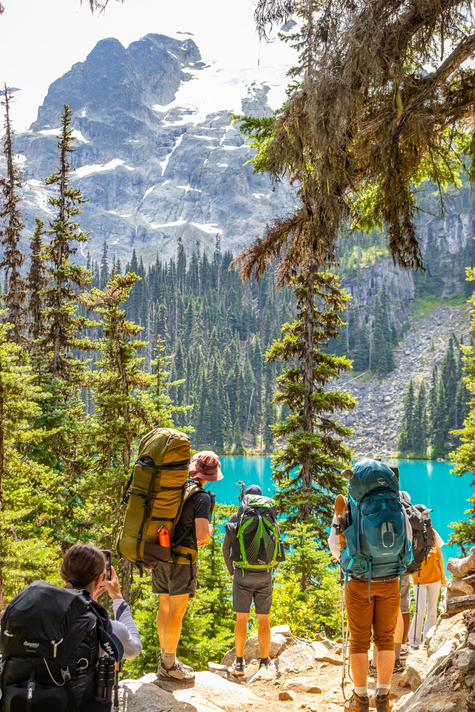 Hikers with backpacks observe a turquoise lake and mountain range.